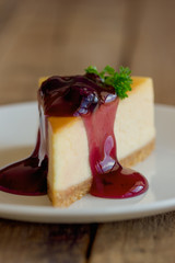 Homemade blueberry cheesecake on white plate decorated with parsley and blueberry sauce. Moist and smooth classic baked cheesecake. Copy space background of delicious blueberry New York cheesecake.