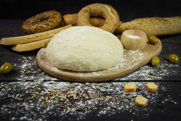 Dough on a wooden board with snacks set and olives in the background