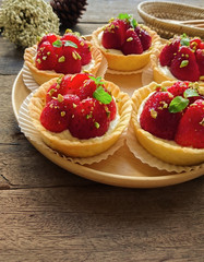 Homemade strawberry tart in paper cup on wood plate. Fruit tart or strawberry tart sprinkle with chopped pistachio and decorated with mint leaf. Delicious strawberry tart on rustic wood background.