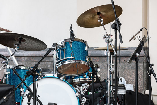 blue drum set and cymbals standing on outdoor stage against wall background