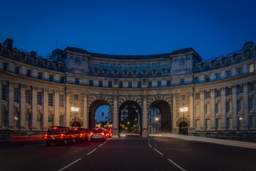Admiralty Arch at night with light trails from passing cars there is a red trail on the left side and a white one on the right side near Trafalgar Square in London as the entrance to The Mall