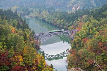 First bridge and Tadami river in beautiful autumn season with train crossing the bridge.