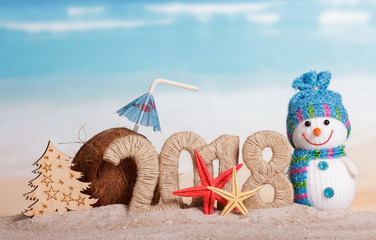 New Year inscription 2018, snowman, Christmas tree, coconut with straw and umbrella, starfish on the sand.