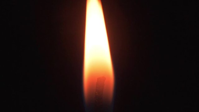 Burning candles on a black background: flame of a candle, ignition of candle. Unknown ignites wick of a candle against a black background. Candle burns in dark. Concept fire, flame, heat, lighter.
