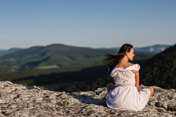 Fototapeta na wymiar Beautiful girl remains on top of a mountain and looks at the horizon with a beautiful background. A colorful photo of a natural sunset, a miracle, incredible, a dance, hair in the wind