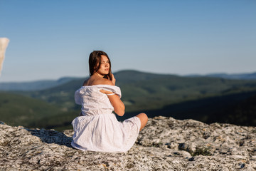 Fototapeta na wymiar Beautiful girl remains on top of a mountain and looks at the horizon with a beautiful background. A colorful photo of a natural sunset, a miracle, incredible, a dance, hair in the wind