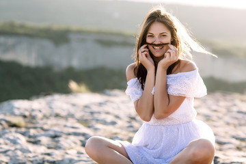 Beautiful girl remains on top of a mountain and looks at the horizon with a beautiful background. A colorful photo of a natural sunset, a miracle, incredible, a dance, hair in the wind