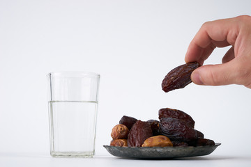 Dates in palm of hand ready to serve for Iftar. Conceptual photo of Ramadan food. Ramadan activities, dates, glass of water isolated on white background with copy space.