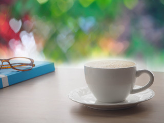 wood office table with latte coffee cup and modern eyeglasses on blue book  cover, beautiful heart shape bokeh texture background, concept of coffee break.