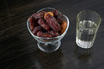 Glass bowl full of dry dates and glass of water for iftar on black wooden table for ramadan month. Islamic religion concept.