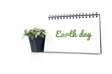 Green earth day text on Desktop calendar and small garden tree on flowerpot on isolated white background.