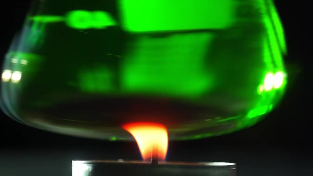 Chemical experiments with ignition of reagents: glass flask with chemical fluid is held over fire. Candle burns and heats the chemical reagent. Heating of chemical flask.