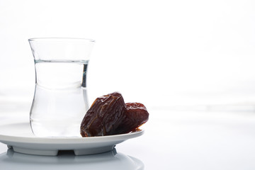 A glass of water and iftar dry dates on white saucer ready to eat for iftar time. Islamic religion and ramadan concept.  White background with copy space.