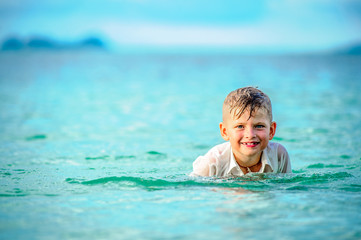 Fototapeta na wymiar As if a bird: a close-up portrait of a handsome boy in wet slim fit shirt jumps and flutters over the water, a lot of splashes and fun. Toothless smile and dancing