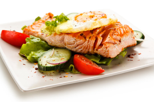 Grilled salmon with fried egg and vegetables on white background 