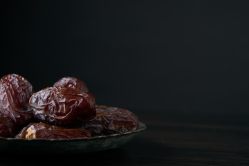 Close-up of Ramadan dates or kurma for iftar opening on silver plate on balck wooden table. Copy space. Islamic religion and ramadan month concept.