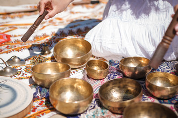 Woman playing a singing bowls also known as Tibetan Singing Bowls, Himalayan bowls. Making sound massage at beautiful sunny day.