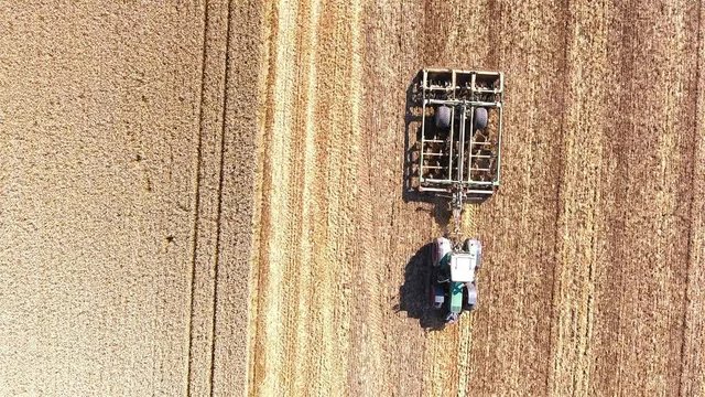 Flying above tractor plowing field on sunny day 4K