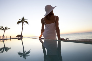 femme assise seule au bord d'une piscine à la mer au coucher du soleil