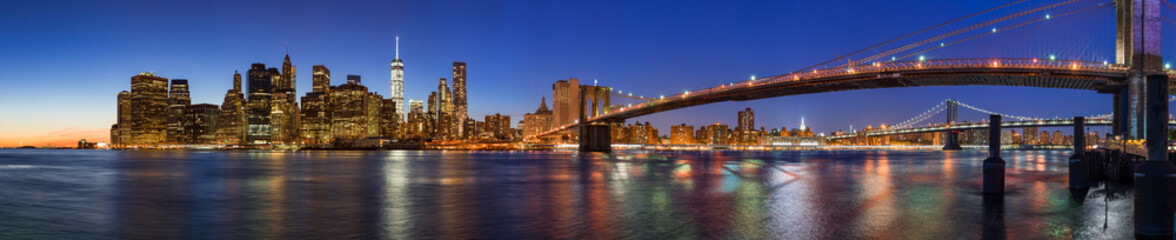 Panoramic view of Lower Manhattan Financial District skyscrapers at twilight with the Brooklyn Bridge and the East River. New York City