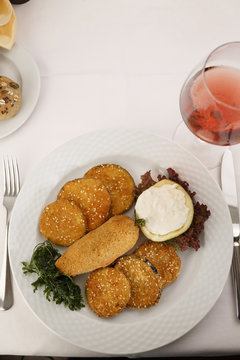 Breaded and fried red bell pepper and eggplant arranged on a plate, Wineglass in background, Traditional dish in elegant setting, Selective focus with soft light