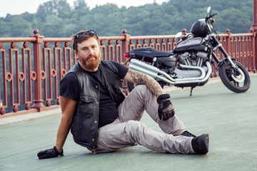 bearded redhead biker with beard in leather jacket sitting on floor.