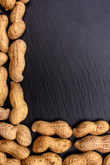 Unclean peanuts lie on a black stone board in the form of a frame, space for text