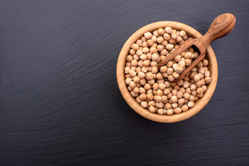On a black stone board there is a wooden scoop and a wooden bowl with chickpeas, place for text