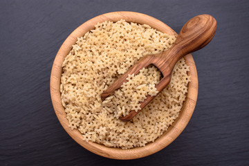 Macaroni in the form of starlets lie in a wooden cup and a wooden scoop on a black stone board, space for text
