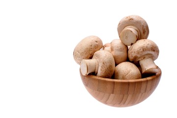 White mushrooms champignons lie in a wooden cup, isolated on a white background