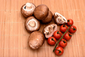 Gray mushrooms champignons and red cherry tomatoes lie on a beech wooden mat