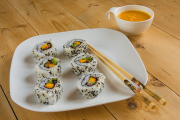 Vegan sushi on plate with sauce on wood table and chopsticks