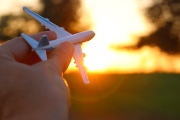 close up of man's hand holding toy airplane against sunset sky