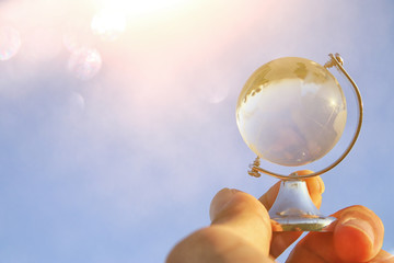 male hand holding small crystal globe in front of blue sky