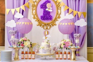 Interior decoration for a child's birthday is one year in purple colors. Candy, macaroon, tiered cake, and juices.