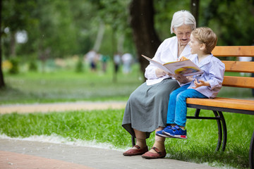 Young boy and great grandmother laughing while reading book in summer park