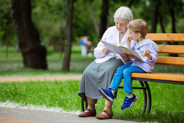 Young boy and great grandmother reading book in summer park