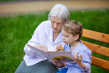 Young boy and great grandmother reading book in summer park