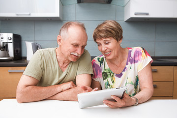 Happy senior couple using tablet in kitchen at home.