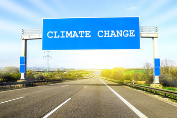 Blue freeway sign over the road on sunny day with words Climate Change on it