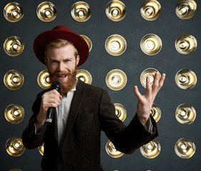 Portrait of stylish extravagant young bearded entertainer announcing next performer during concert,...