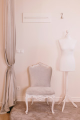 Stylish light dressing room. Elegant soft armchair placed over beige wall near white dummy. Pastel interior of dressing room