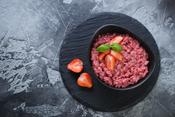 Risotto with strawberries served in a black bowl, top view on a grey stone background, copyspace