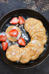 Above view of fritters with strawberries and powdered sugar served on a metal plate, studio shot