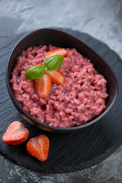 Risotto with strawberries served in a black bowl on a stone slate tray, selective focus, studio shot