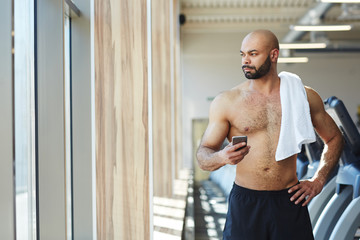 Attractive athlete with towel and smartphone messaging in gym