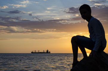 Silhouette of the ship over the sunrise and silhouette of the teenager