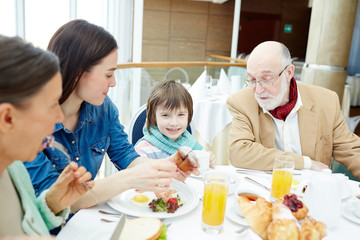 Obraz na płótnie Canvas Happy family sitting by table and having breakfast