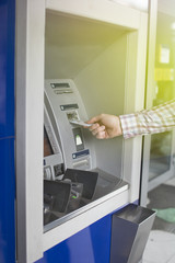 Hand of a man with a credit card, using an ATM. Man using an atm machine with his credit card. Closeup of male hands using smart phone while typing on ATM.
