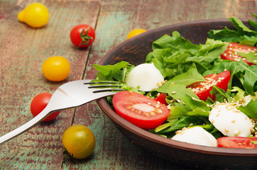 Green salad made with arugula, tomatoes, cheese mozzarella balls and sesame on plate